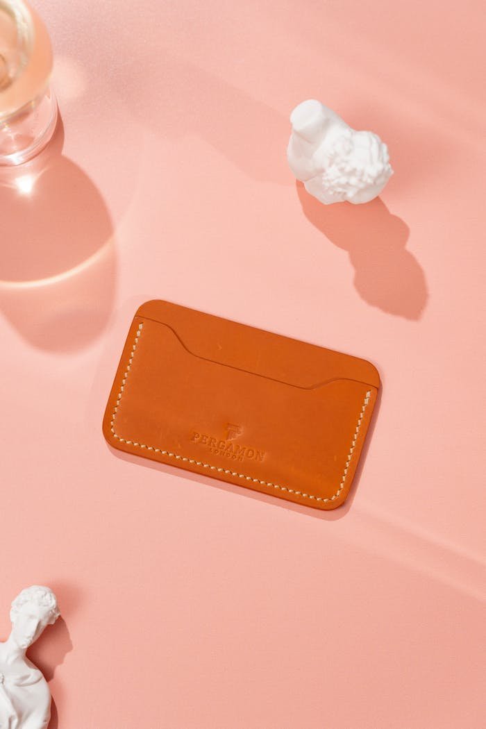 Minimalist leather card holder on pink background with decorative elements.