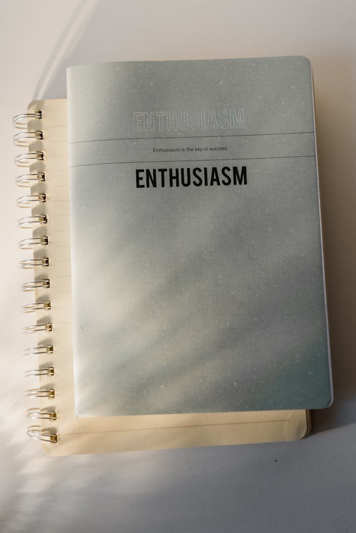 Top view of a minimalist notebook with 'Enthusiasm' printed on the cover, on a white background.